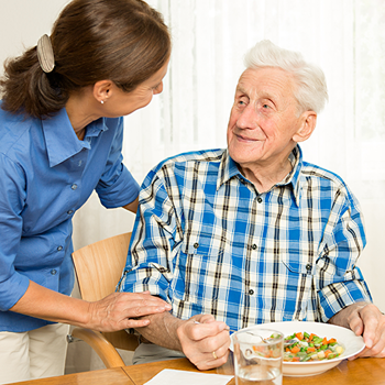 Female caretaker assisting an elderly man with his meal.